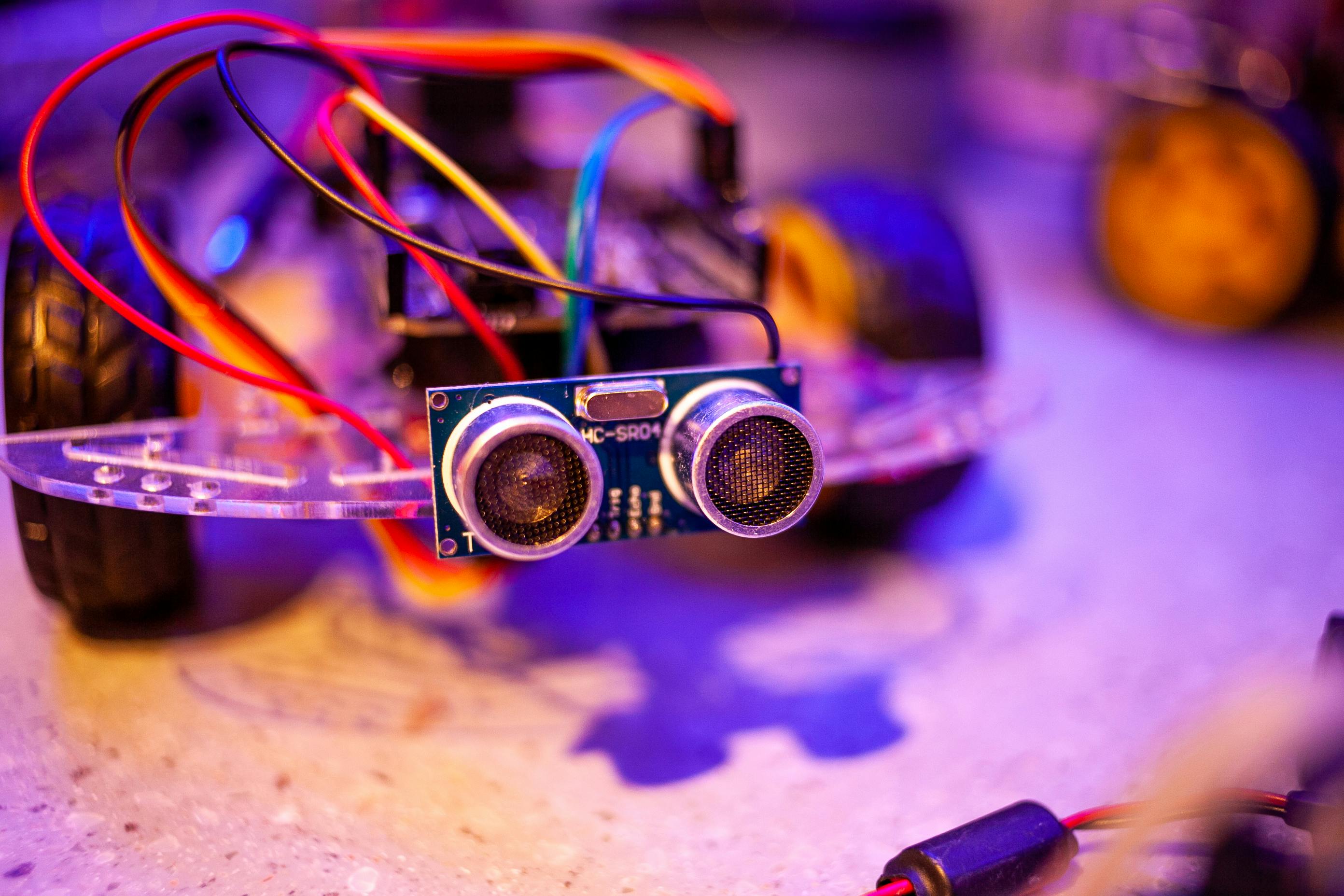 Close-up of a DIY robot car project with an HC-SR04 ultrasonic sensor, colorful wires, and microcontroller on a workbench.